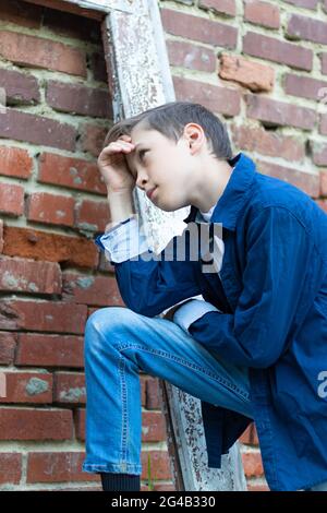 Ein modisch gekleideter Kerl in einem blauen Hemd steht an einer alten verwitterten Tür gegen eine Ziegelwand. Nahaufnahme. Selektiver Fokus. Hochformat Stockfoto