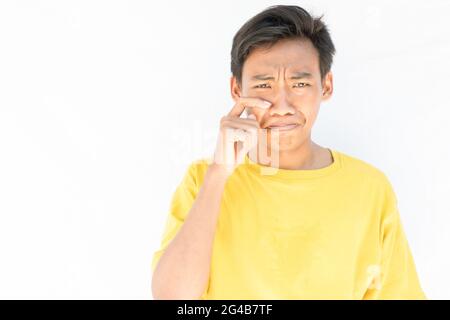 Ein Indonesier mit einem gelben T-Shirt, der die Tränen auf weißem Hintergrund von seinem Gesicht abwischt Stockfoto