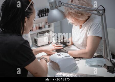Frau in einem Nagelstudio erhält eine Maniküre von einer Kosmetikerin mit Nagelfeile. Frau bekommt Nagelmaniküre. Kosmetikerin feilen Nägel an einen Kunden. Stockfoto