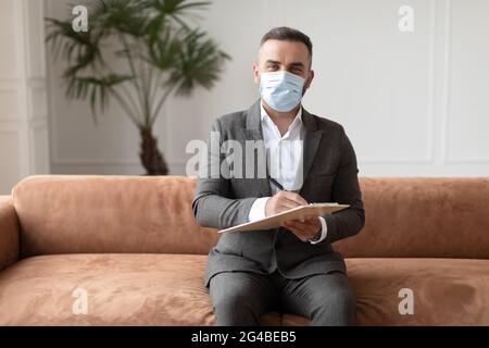 Porträt eines professionellen Therapeuten in Maske auf dem Sofa sitzend Stockfoto