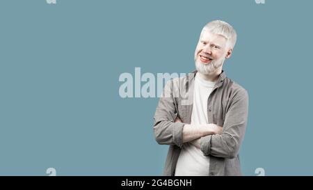 Positiver Albino-Typ mit gefalteten Armen, der die Kamera anschaut und lächelt, türkisfarbener Hintergrund mit leerem Raum, Panorama Stockfoto