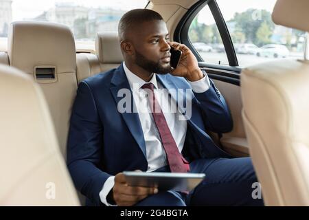Wohlhabender schwarzer Manager, der im Auto sitzt und ein digitales Tablet verwendet Stockfoto