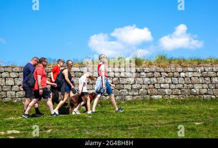 Menschen und Familien, die entlang eines Abschnitts der clayton-Mauer auf dem Rasen wandern, während sie auf dem nationalen Fernwanderweg Hadrians Wall spazieren Stockfoto