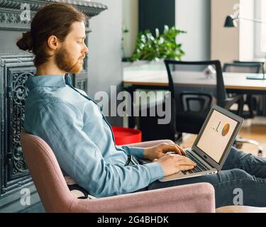 Junger, fokussierter Mann, der an einem Laptop arbeitet Stockfoto