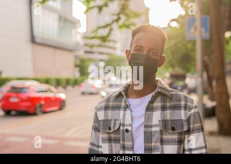 Schöner und modischer afrikanischer schwarzer Mann im Sommer in der Stadt trägt Gesichtsmaske hinten beleuchtet Aufnahme mit Linse Flare Stockfoto