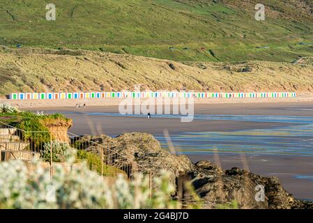 Weiße Strandhütten, mit farbigen Türen, stehen vor Dünen mit Reflexen im feuchten Strandsand am Woolacombe Beach, Devon Stockfoto