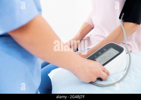 Die junge Frau lässt ihren Blutdruck von einer Krankenschwester, einem Arzt oder einem Gesundheitsgast überprüfen. Herzgesundheit. Digitaler Blutdruckmessgerät. Stockfoto