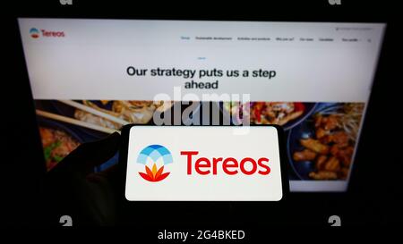 Person, die Mobiltelefon mit dem Logo des französischen Landwirtschaftsunternehmens Tereos S.A. auf dem Bildschirm vor der Business-Webseite hält. Konzentrieren Sie sich auf die Telefonanzeige. Stockfoto
