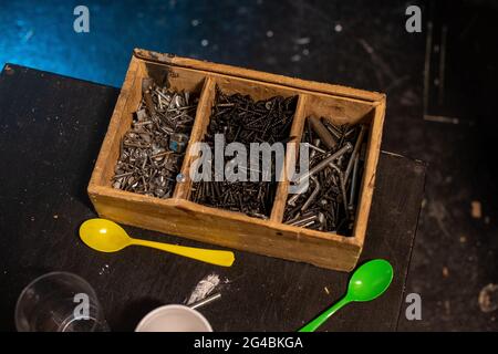 Eine Nahaufnahme von Schrauben, Muttern und Schrauben in einem Holzfach mit Kunststofflöffeln auf dem Tisch Stockfoto
