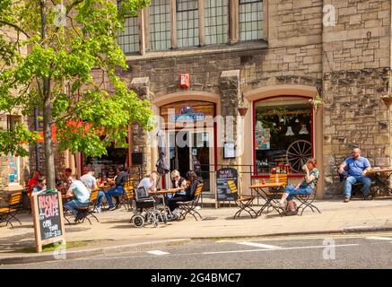 Leute, die draußen sitzen und die Sonne genießen, essen und trinken in einem Straßencafé in der Marktstadt Hexham England Stockfoto