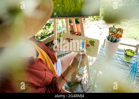 Junge Künstlerin arbeitet an ihrer Kunst Leinwand Malerei im Freien in ihrem Garten. Achtsamkeit, Kunsttherapie, Kreativität und kreative Hobbys Konzept. Stockfoto