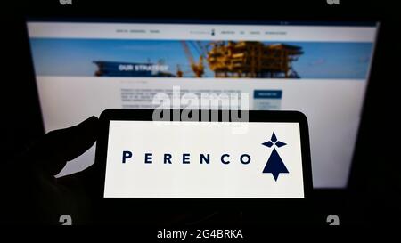 Person, die ein Mobiltelefon mit dem Logo des anglo-französischen Öl- und Gasunternehmens Perenco S.A. auf dem Bildschirm vor der Webseite hält. Konzentrieren Sie sich auf die Telefonanzeige. Stockfoto