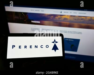 Person, die Mobiltelefon mit dem Logo des anglo-französischen Öl- und Gasunternehmens Perenco S.A. auf dem Bildschirm vor der Business-Webseite hält. Konzentrieren Sie sich auf die Telefonanzeige. Stockfoto