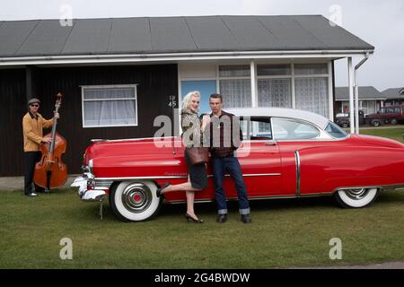 GROSSBRITANNIEN / England /Norfolk /Hemsby Rock 'N' Roll Weekender. Ein Paar und ein Kontrabasser posieren neben einem roten cadillac. Stockfoto