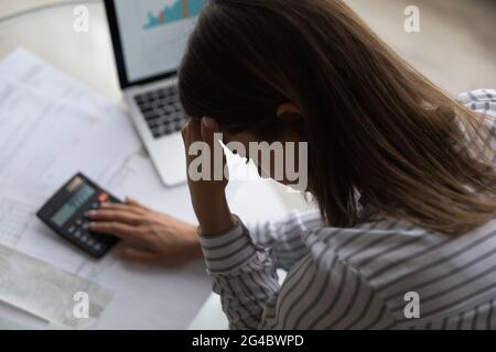 Frustrierte, unglückliche junge Frau, die die Ausgaben in Innenräumen berechnet. Stockfoto