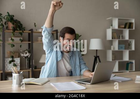 Emotionaler junger Mann, der den Erfolg des Internets zu Hause feiert. Stockfoto