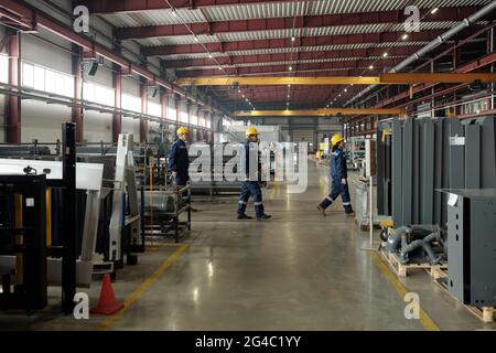 Gruppe von Fabrikmitarbeitern in Harthüten und blauer Arbeitskleidung, die in der Industrie in einer Linie zwischen Kompressoreinheiten laufen Stockfoto
