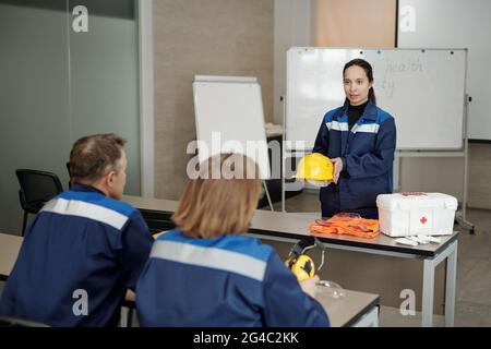 Attraktive Frau mit gemischter Rasse, die gelben Hut in der Hand hält und den Mitarbeitern von der persönlichen Sicherheit in der Industrie erzählt Stockfoto