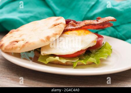 Ein Frühstückssandwich mit knusprigem Speck, farmfrischem Ei, Tomaten und Salat Stockfoto