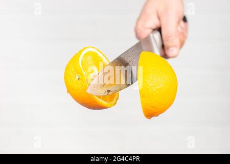 Der Mann schneidet eine Orange im Flug auf einem Backstein weißen Wand Hintergrund Stockfoto