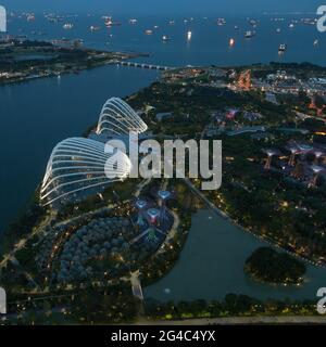 Blick auf die Gärten von Singapur an der Bucht, wenn die Sonne untergeht und die Lichter aufgehen, mit vielen Schiffen in der geschäftigen Straße von Singapur dahinter Stockfoto