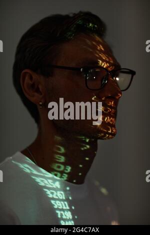 Dunkles Porträt eines jungen Mannes in einer Brille mit Computercode im Gesicht Stockfoto