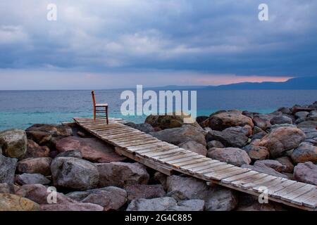 Holzstuhl auf der Holzterrasse auf den Felsen entlang der Ägäis in der Nähe der antiken Stadt Assos in der Türkei Stockfoto