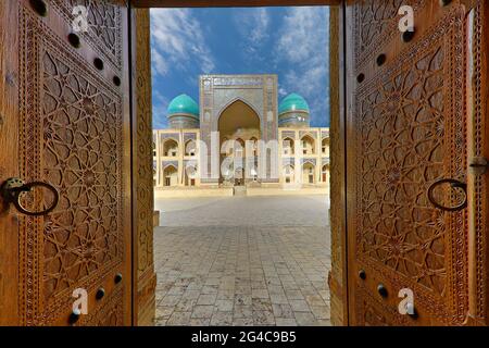 Blick über die theologische Schule von POI Kalon, durch die Holztüren der Moschee in Buchara, Usbekistan. Stockfoto