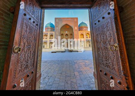 Blick über die theologische Schule von POI Kalon, durch die Holztüren der Moschee in Buchara, Usbekistan. Stockfoto