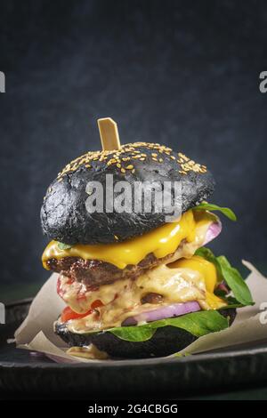 Double Beef Patty Burger mit einem schwarzen Brötchen auf dunklem Hintergrund Stockfoto