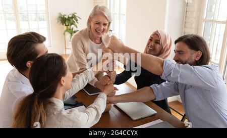 Begeisterte, vom Unternehmenserfolg motivierte, vielfältige Mitarbeiter, die sich im Team mit Fäusten stapeln Stockfoto