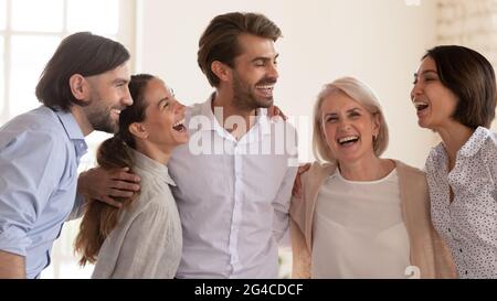 Aufgeregte, multiethnische Geschäftsleute, die lachen und umarmen und den Erfolg feiern Stockfoto