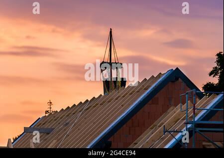 Ein Dachstuhl eines neuen Gebäudes mit einem Richtkranz bei Sonnenuntergang Stockfoto