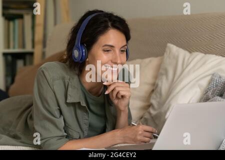 Nahaufnahme einer lächelnden Frau in Kopfhörern mit einem Laptop, die sich Notizen macht Stockfoto