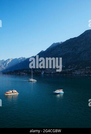 Ein Blick auf Montenegro von den Gewässern der Adria. Drei Boote schweben vor der Küste, und Dörfer können entlang der bergigen Klippe gesehen werden Stockfoto