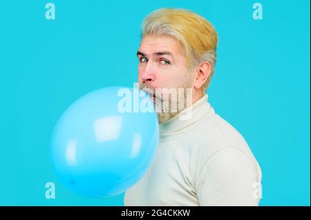 Alles Gute zum Geburtstag. Stilvoller bärtiger Mann bläst blauen Luftballon. Attraktive männliche aufblasende Ballon Vorbereitung für Party Stockfoto