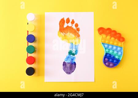 Neue trendige beliebte Silikon bunte Anti Stress Pop IT Spielzeug für Kinder und bunte Fußabdruck auf gelbem Hintergrund. Stockfoto
