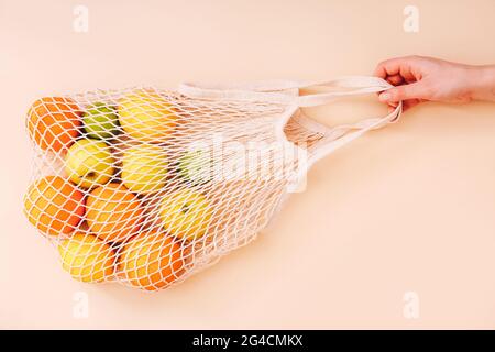 Weibliche Hand hält Mesh Eco-Tasche mit Früchten auf hellem Hintergrund. Gesunde, saubere Ernährung. Eco-Shopping-Konzept. Stockfoto