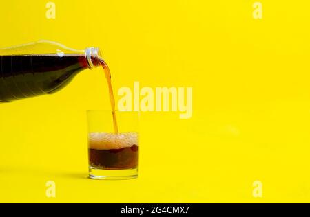 Schwarze Limonade in das Glas gegossen, Flasche Soda isoliert auf Farbhintergrund Stockfoto