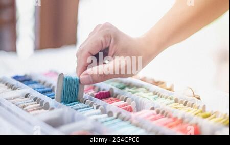 Nahaufnahme Hände der Schneiderin mit ozeanblauen Fäden und verschiedenen Farben in der Box auf den Tisch gelegt und bereiten Sie sich auf die Verwendung mit weißer Baumwolle. Stockfoto