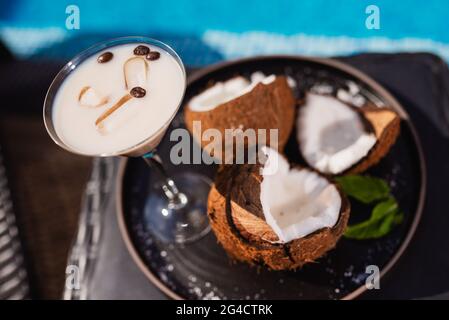 Blick von oben auf den Kaffee in einer Tasse mit Bohnen und Eis, serviert auf einem Tablett neben der Kokosnuss. Erfrischungen am Pool Stockfoto