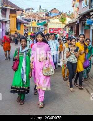 Zwei attraktive Mädchen, die die große Gruppe indischer Schulkinder in farbenfrohen Kleidern anführen, gehen durch die Straßen Gokarna, Karnataka, Indien Stockfoto