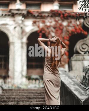 Junge schlanke Rothaarige Frau im Sommerkleid geht die Treppe in der alten Burg, Palast, hält die Hände am Kopf Stockfoto