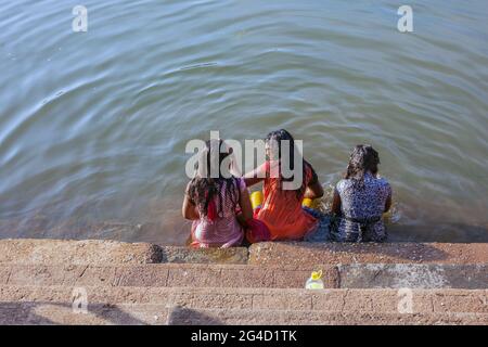 Drei Weibchen sitzen auf den Stufen, die teilweise im Wasser des Koti Tirtha Wassertanks, Gokarna, Karnataka, Indien, untergetaucht sind Stockfoto