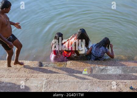 Drei Weibchen sitzen auf den Stufen, die teilweise im Wasser des Koti Tirtha Wassertanks, Gokarna, Karnataka, Indien, untergetaucht sind Stockfoto