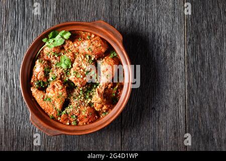 Chakhokhbili, geschmortes Huhn, Tomate mit frischen Kräutern, Walnüssen und Gewürzen in einem Tontopf auf einem Holztisch, georgisches Gericht, flaches Lay, Freiraum Stockfoto