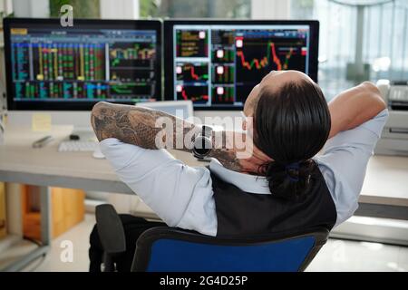 Glücklicher erfolgreicher Händler, der sich nach einem glücklichen Arbeitstag in seinem Sessel entspannt Stockfoto