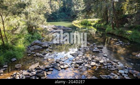 Licht und Schatten auf seichtem Wasser, das über Felsen in einem Bach im australischen Busch fließt Stockfoto