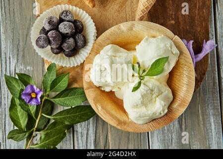 Vanilleeis in Tasse auf Holzbrett mit Beeren und Blumen Stockfoto