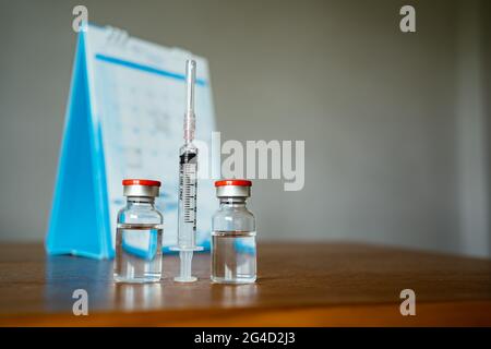 2 Impfstofffläschchen, Spritze und ein Kalender im Hintergrund Stockfoto